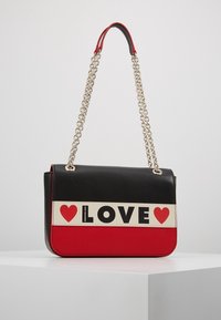 Černá a červená kabelka s řetízkem, která má krémový pruh s nápisem "LOVE" tučným černým písmem a ikonami červeného srdce. Hladký povrch.