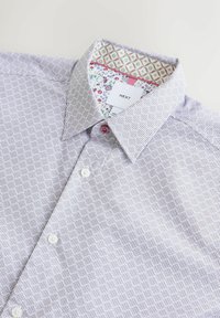 Chemise violette claire à motifs avec un col structuré, dotée de boutons blancs et d'une doublure intérieure contrastante à motifs floraux et géométriques.