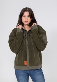 Zielona oliwkowa kurtka polarowa o teksturowym wykończeniu. Posiada napy, kontrastowe szare akcenty oraz metkę w pobliżu dołu.