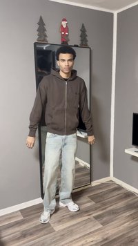 Ruskea vetoketjullinen huppari, vaaleansiniset leveälahkeiset farkut ja harmaat lenkkarit. Seistään peilin edessä, jonka takana on seinä, joka on koristeltu joulukoristeilla.