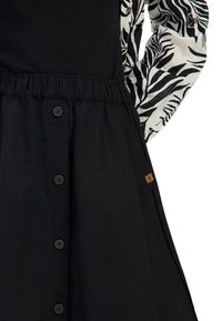 Zwarte jurk met een aangesloten taille, knoopdetails en mouwen met een zebra-patroon. Materiaal is stof met een zachte textuur. Bruine logo-accent.