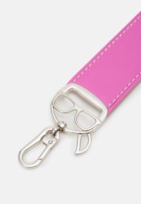 Bracelet en cuir rose avec fermoir en métal argenté en forme de visage portant des lunettes et une écharpe, attaché à un crochet clip.