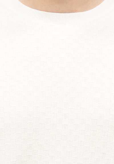 Κοντινή λήψη λευκού πλεκτού πουλόβερ με υφή και διακριτικό σχέδιο ψάθας με στρογγυλή λαιμόκοψη σε ανοιχτόχρωμο δέρμα.