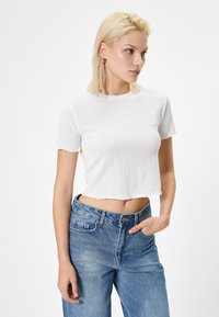 Biały prążkowany crop top z krótkim rękawem, z okrągłym dekoltem. W zestawie z niebieskimi dżinsami z wysokim stanem.