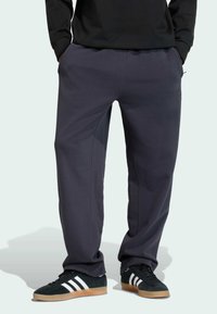 Mørkegrå joggingbukser med elastisk taljebånd, sidelommer og ton-i-ton syninger. Parret med sorte sneakers med hvide striber.