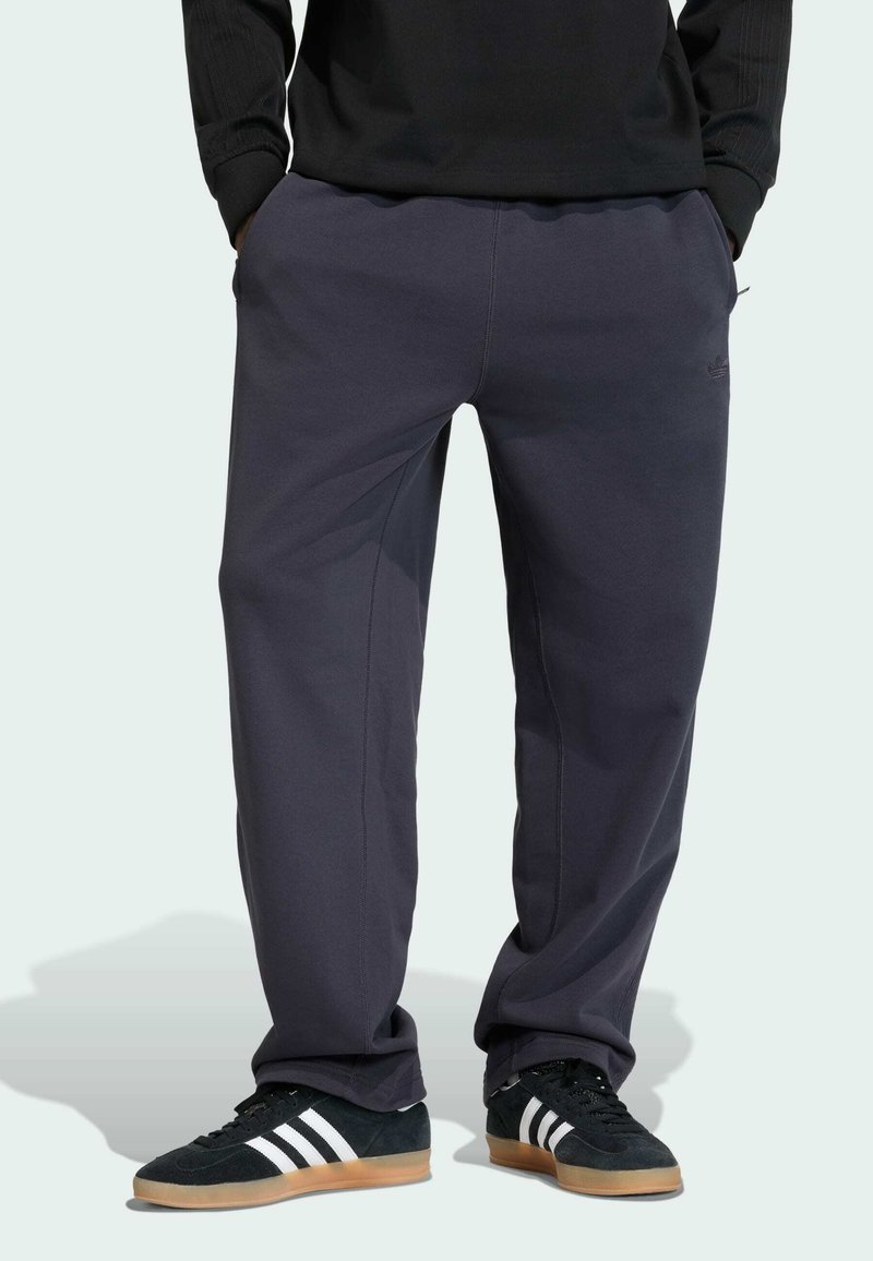 Mørkegrå joggingbukser med elastisk taljebånd, sidelommer og ton-i-ton syninger. Parret med sorte sneakers med hvide striber.