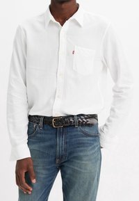 Witte lange mouwen shirt met een enkele borstzak, button-down kraag, gecombineerd met blauwe denim jeans en een zwarte gevlochten riem.