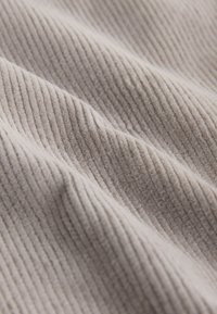 Tissu en velours côtelé beige avec des nervures douces, semblables à du velours, disposées en lignes parallèles et plis délicats.