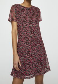 Robe à manches courtes, longueur genou en tissu noir avec un motif floral rouge. Texture légère et translucide, encolure ronde, silhouette fluide.