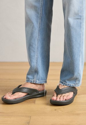 Infradito neri in gomma con una fascia a forma di Y, superficie testurizzata e perforazioni, indossati con jeans azzurri chiari leggermente sfilacciati all'orlo.