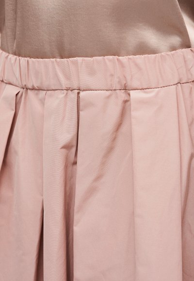 Φούστα ροζ ανοιχτού χρώματος με πιέτες και ελαστική ζώνη μέσης, κατασκευασμένη από λείο ύφασμα με απαλή υφή και μικρή λάμψη.