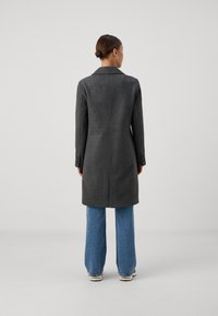 Caban gri din lână cu o croială ajustată, design cu un singur rând de nasturi și rever în formă de ușă, asortat cu blugi largi de culoare albastru deschis.