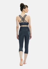 Donkergrijze sportbh met kruislings rugbanden en bijpassende cropped legging. Glad textuur; aansluitend ontwerp; enkel-lengte; subtiele merkdetail.