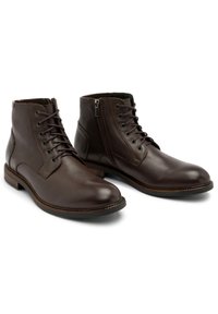 Brązowe skórzane botki za kostkę o gładkim wykończeniu, zawiązywane z przodu, z bocznym zamkiem błyskawicznym i teksturowaną podeszwą. Posiadają kontrastujące szwy i zaokrąglony czubek.