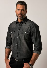 Camicia in denim nero con colletto a bottoni, doppie tasche frontali e bottoni bianchi. Tessuto testurizzato e maniche lunghe arrotolate.
