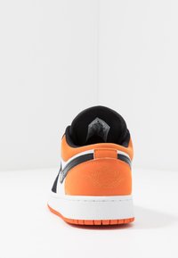 Sneaker arancione e nero con suola bianca. Presenta una parte superiore in suede, logo ricamato sul tallone e un colletto imbottito per il comfort.