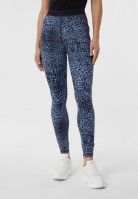 Leggings stampati in blu e nero con motivo leopardato, dotati di una vita alta e un tessuto liscio e elasticizzato. Abbinati a sneakers bianche.