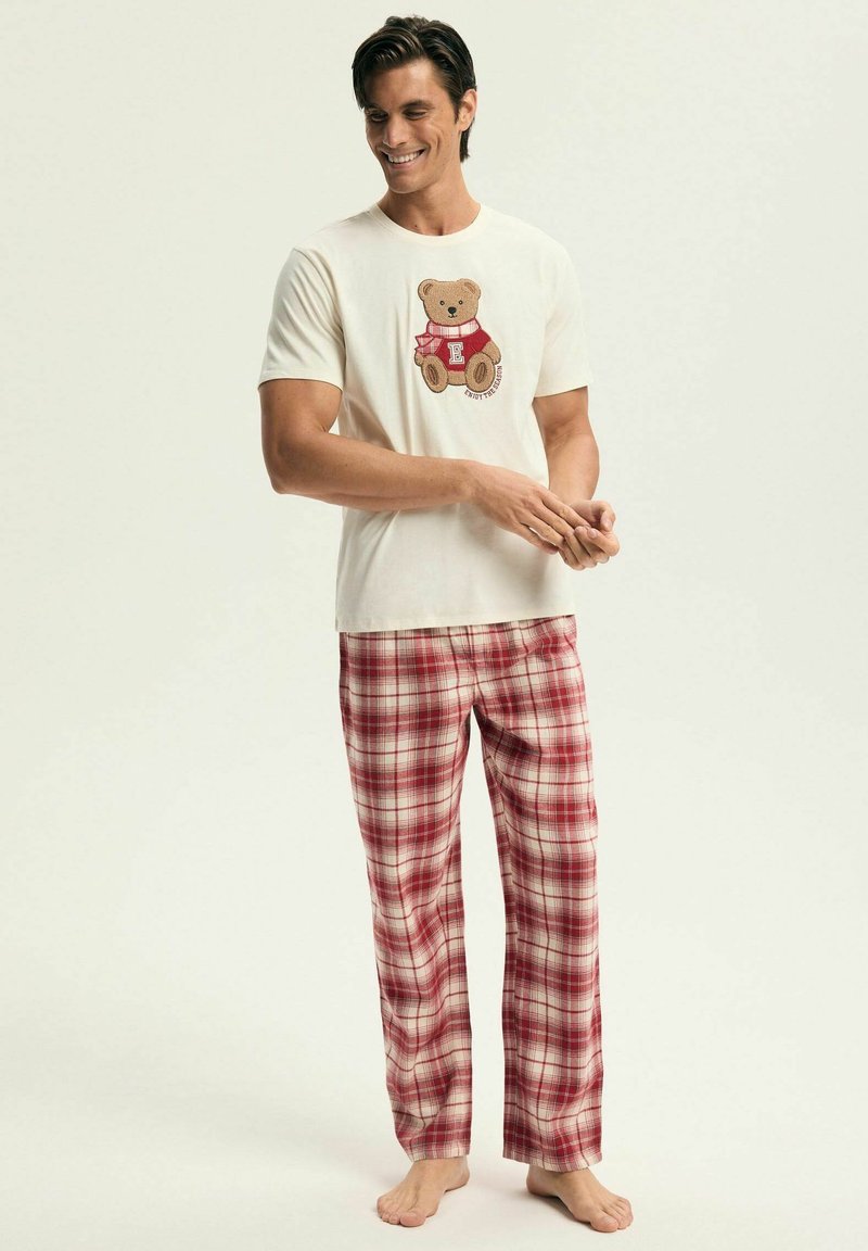 Kremowy T-shirt z grafiką misia, w połączeniu z luźnymi czerwono-białymi spodniami w kratę; oba wykonane z miękkiej bawełny.