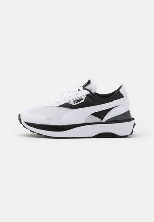 Hvid og sort Puma-sneakers med mesh- og læderoverdel, snøredesign og tyk sål vist i venstre profil på en hvid baggrund.
