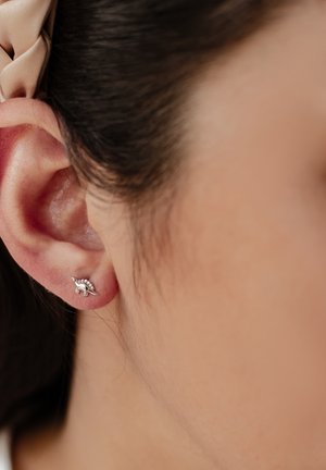 Silberner Steckerohrring in Form eines kleinen Dinosauriers, mit feiner Detailarbeit und glänzendem Finish, der an einem Ohr einer Person getragen wird.