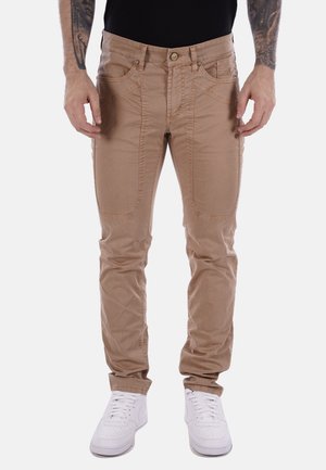 Pantaloni beige dalla vestibilità aderente, con tasche frontali e una texture liscia, abbinati a sneakers bianche.