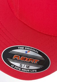 Red cap made of textured fabric, featuring a round black label with silver and orange text, stating "FLEXFIT S/M" at the side.