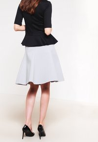 Top peplum negro con mangas cortas, combinado con una falda gris a la altura de la rodilla. El modelo lleva zapatos de tacón alto negros. Texturas suaves, diseño elegante.