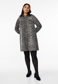 Vestido camisero de estampado de leopardo en tejido suave, con botones en la parte delantera, dos bolsillos en el pecho y un corte relajado, combinado con medias negras y tacones.