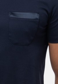 Marinblå t-shirt med kort ärm som har en rektangulär bröstficka med satinaccent, tillverkad av mjukt, elastiskt bomullstyg.