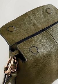 Oliivirohelise nahast käekott tekstureeritud viimistlusega, magnetilise kinnituse ja roosakaskuldsed riistvaradetailid. Sisemus on nähtav ava kaudu.