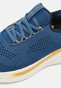 Niebieski sportowy but z siateczki, charakteryzujący się teksturowaną cholewką, pomarańczowymi sznurówkami i białą podeszwą pośrednią z złotą linią.