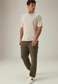 Tricou bej cu mânecă scurtă, asortat cu pantaloni cargo verzi măslinii, cu buzunare laterale, completat de adidași albi și negri.