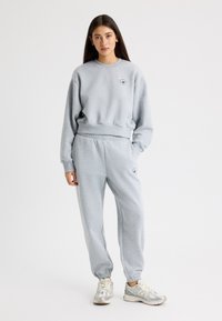 Sudadera gris y joggers a juego hechos de tela suave. La sudadera tiene un cuello redondo y un detalle de logo; los joggers tienen puños y cintura elásticos.