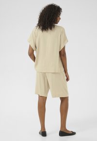 Haut beige à manches courtes et short assorti en tissu léger. Coupe décontractée, design uni, avec une esthétique minimaliste. Chaussures plates noires.