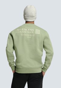 Lichtgroene sweatshirt met een ronde hals en ribgebreide manchetten. Kenmerkend zijn de witte grafische tekst op de achterkant, de gladde structuur en de ontspannen pasvorm.
