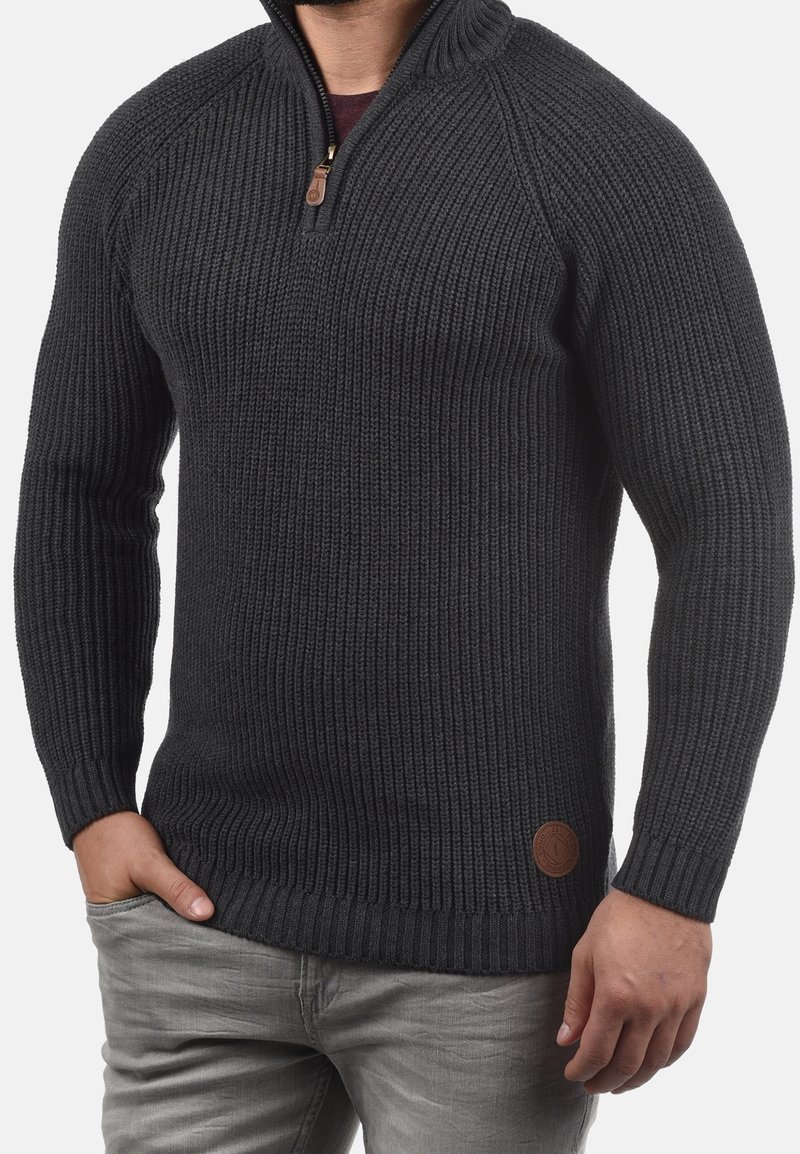 Maglione lavorato a maglia di colore grigio scuro con texture a coste, collo con mezza cerniera e dettaglio in pelle nell'angolo inferiore sinistro. Maniche lunghe, forma aderente.