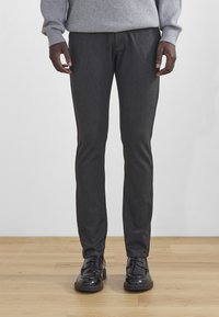 Temno sivi krojeni hlače iz teksturiranega materiala, s slim fit krojem in gladko površino. Poudarjene s črnimi usnjenimi čevlji.