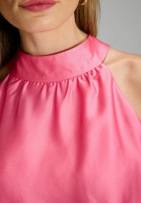 Haut en satin rose à licou avec un tissu froncé au cou, texture lisse et col haut, offrant un drapé élégant et des bords nets.