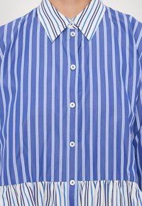 Chemise à rayures verticales bleues et blanches, à boutons, col pointu et détail froncé à l'ourlet à la taille.