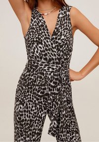 Jumpsuit en imprimé léopard noir et blanc avec un décolleté en V profond, des bretelles larges et une taille nouée. Tissu léger avec une texture lisse.