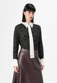 Black blouse with white diamond pattern, white collar and tie detail, paired with a burgundy leather skirt, smooth texture, long sleeves.