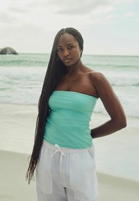 Een turquoise strapless top gecombineerd met witte linnen broek. De top heeft een gladde textuur, en de broek heeft een trekkoord in de taille.