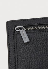 Portafoglio in pelle nera texturizzata con zip e accessori in argento. Presenta un'etichetta con il logo attaccata al tirazip.