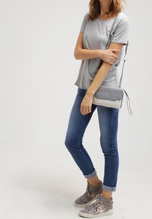 T-shirt grigio, jeans skinny blu e sneakers alte grigie con paillettes. Indossa una piccola borsa a tracolla grigia con accenti testurizzati.