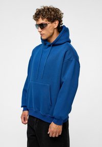 Sweatshirt à capuche bleu avec une poche avant, des poignets côtelés et une coupe décontractée. Fabriqué à partir d'un tissu doux, avec une texture lisse.