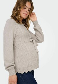 Svetlo siva kardigan z strukturiranim pletenim vzorcem, gumbi za zapiranje in zavezanim pasom. Ima rebraste manšete in valovit rob.