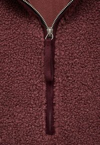 Pullover de medio zip de forro polar burdeos con superficie texturizada, que presenta un zipper de metal y un interior suave.
