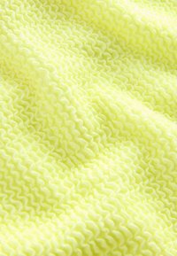Textúrovaná látka v jasne žltej farbe s vlnitým vzorom. Materiál vyzerá ľahko a elasticky, s výraznými vlnkami rozmiestnenými po celej ploche.