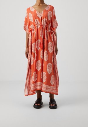 Robe caftan corail à motifs de feuilles blanches, décolleté en V, taille élastique avec détail à pompons, manches courtes et silhouette fluide. Sandales noires.