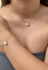 Silberne Kettenhalskette und passendes Armband mit einem einzelnen runden weißen Perlenanhänger. Glatte Textur und minimalistisches Design, auf der Haut getragen.